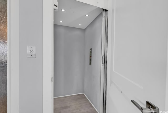 bathroom featuring elevator, baseboards, wood finished floors, and recessed lighting