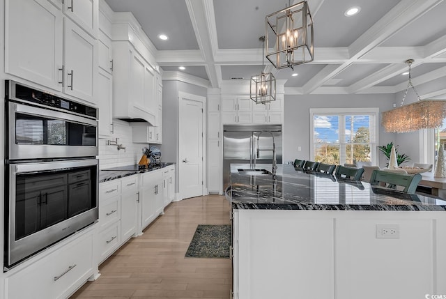 kitchen with a spacious island, coffered ceiling, white cabinets, appliances with stainless steel finishes, and tasteful backsplash