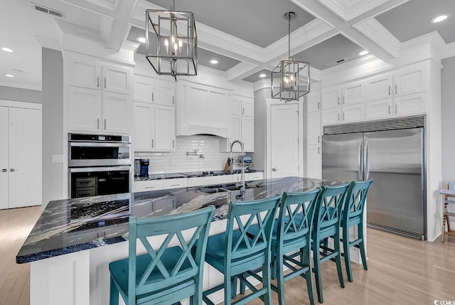 kitchen with light wood finished floors, appliances with stainless steel finishes, decorative backsplash, and a notable chandelier