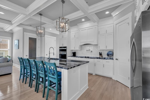 kitchen featuring stainless steel appliances, a sink, custom exhaust hood, backsplash, and light wood finished floors