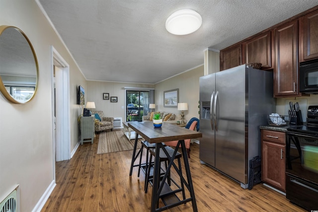 kitchen featuring open floor plan, black appliances, a textured ceiling, and wood finished floors