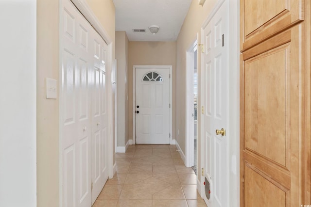 hall with light tile patterned floors, visible vents, and baseboards