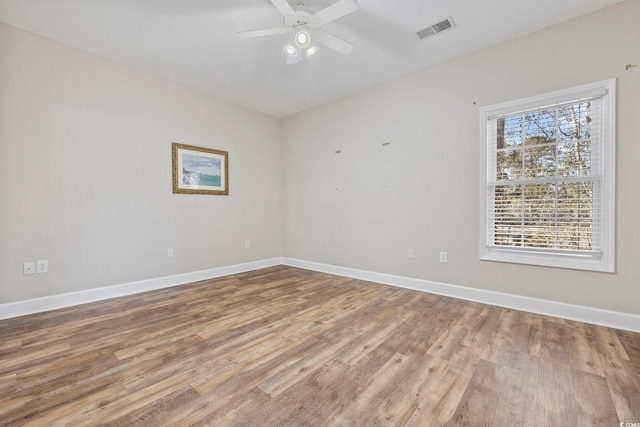 empty room with wood finished floors, visible vents, and baseboards