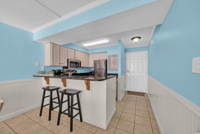 9400 Shore Dr Unit 722, Myrtle Beach, SC 29572 - kitchen with appliances with stainless steel finishes, a peninsula, a wainscoted wall, light tile patterned floors, and a kitchen bar