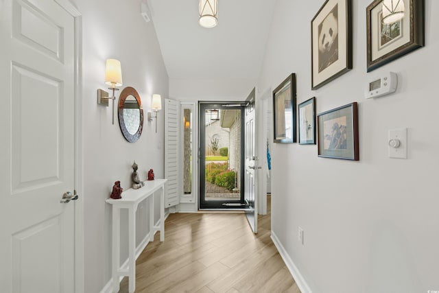 doorway to outside featuring light wood-type flooring, baseboards, and lofted ceiling