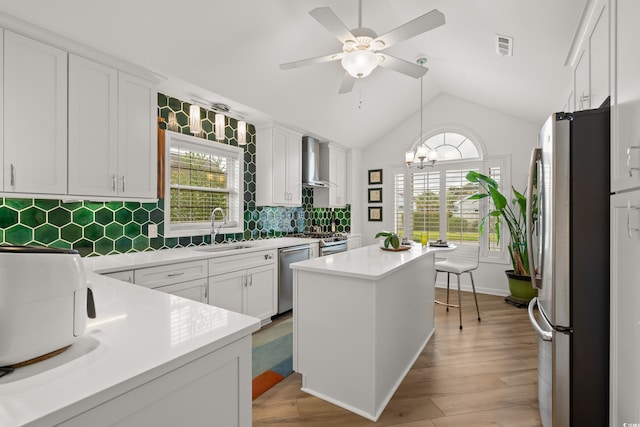 kitchen with wall chimney exhaust hood, a sink, a wealth of natural light, ceiling fan with notable chandelier, and stainless steel appliances