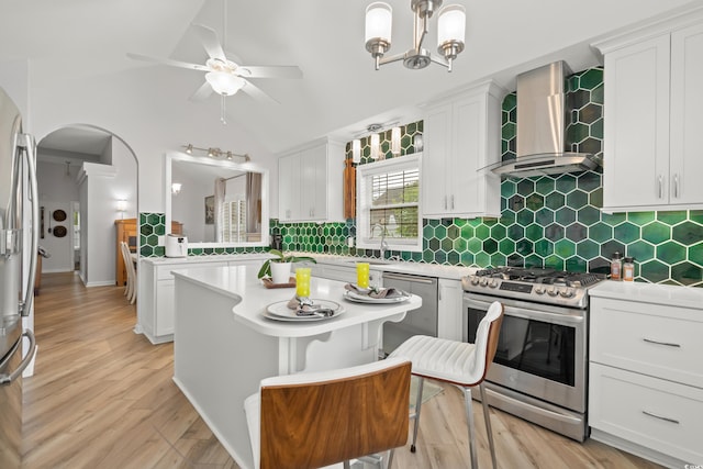 kitchen with light countertops, wall chimney exhaust hood, lofted ceiling, stainless steel appliances, and arched walkways