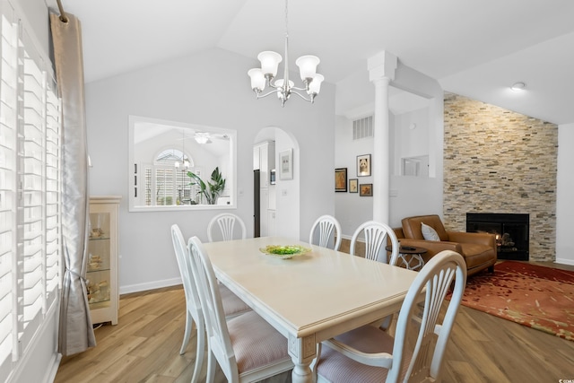 dining space featuring a fireplace, light wood-style flooring, visible vents, vaulted ceiling, and a notable chandelier