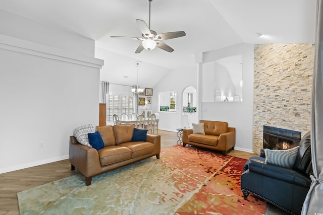 living area featuring baseboards, a fireplace, wood finished floors, ceiling fan with notable chandelier, and lofted ceiling
