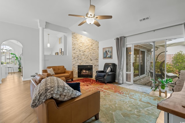 living room featuring a stone fireplace, lofted ceiling, visible vents, and plenty of natural light