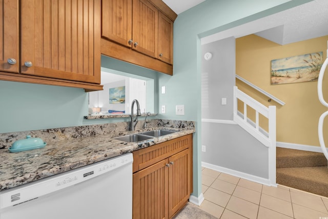 kitchen featuring light stone counters, light tile patterned flooring, white dishwasher, a sink, and baseboards