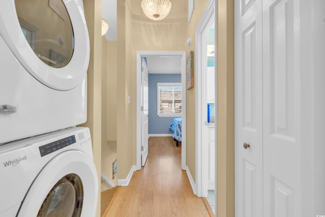 washroom featuring laundry area, stacked washer / dryer, light wood-style flooring, and baseboards