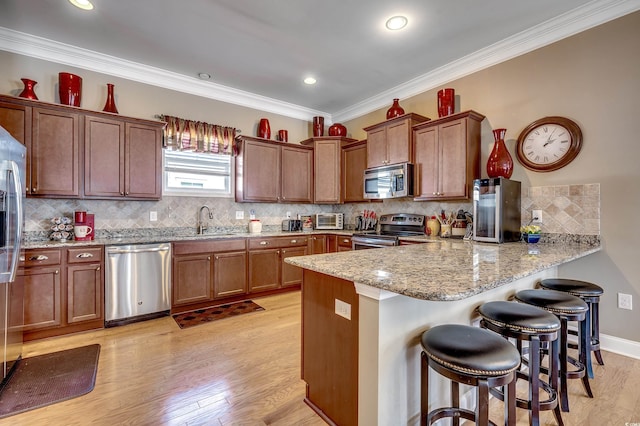 kitchen featuring light wood-style flooring, a peninsula, a sink, a kitchen breakfast bar, and appliances with stainless steel finishes