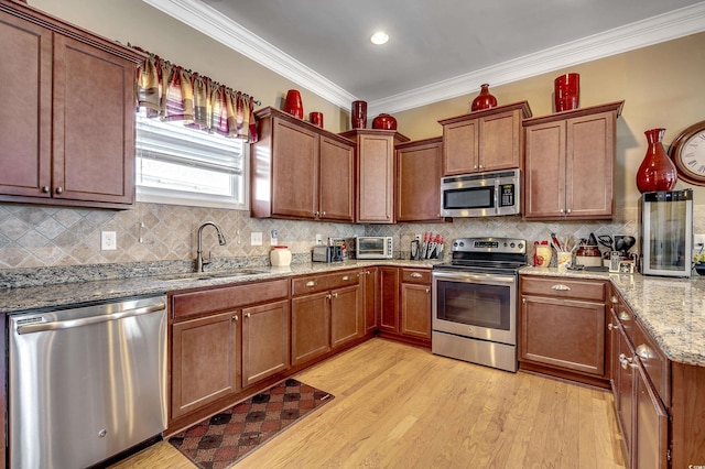 kitchen featuring a sink, stainless steel appliances, crown molding, light wood-style floors, and backsplash