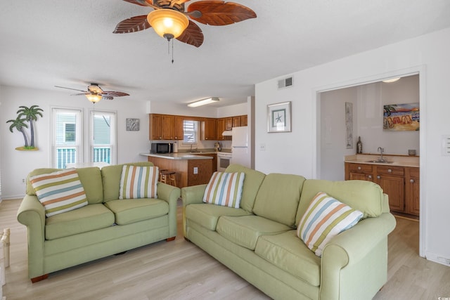 living room with visible vents, light wood-style flooring, baseboards, and ceiling fan