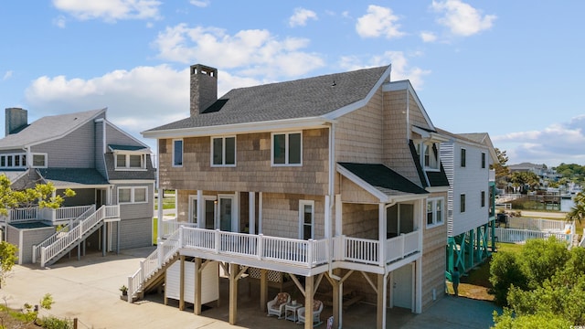 rear view of property featuring concrete driveway, stairway, roof with shingles, and a chimney