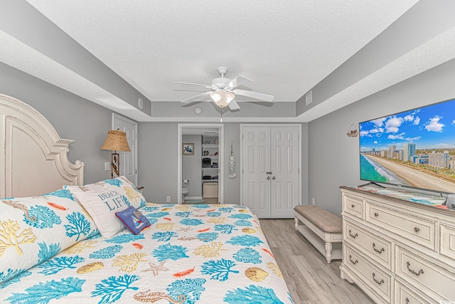 bedroom with a tray ceiling, a closet, ceiling fan, a textured ceiling, and light wood-type flooring