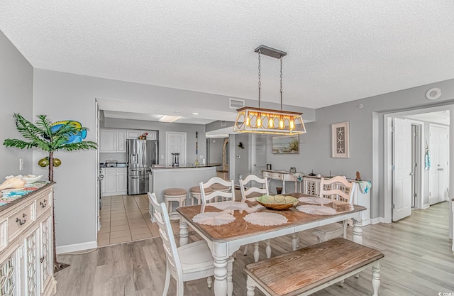 dining room featuring a textured ceiling, light wood finished floors, visible vents, and baseboards