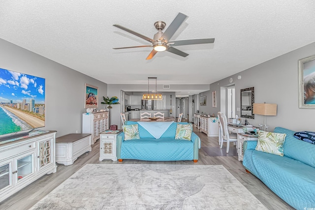 living room featuring light wood-type flooring, ceiling fan, and a textured ceiling