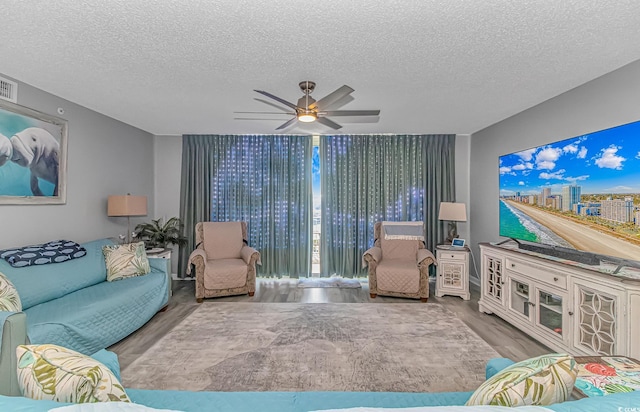 living room featuring a ceiling fan, a textured ceiling, visible vents, and wood finished floors