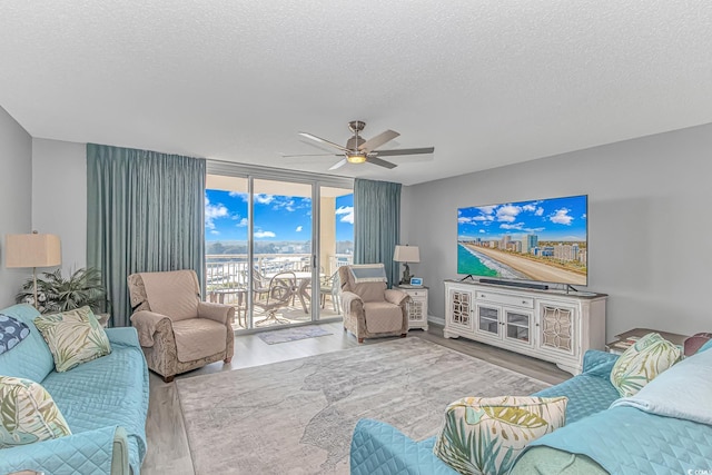 living area with expansive windows, a textured ceiling, wood finished floors, and a ceiling fan