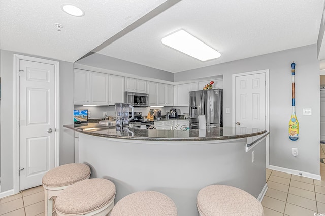 kitchen featuring a textured ceiling, light tile patterned flooring, baseboards, white cabinets, and appliances with stainless steel finishes