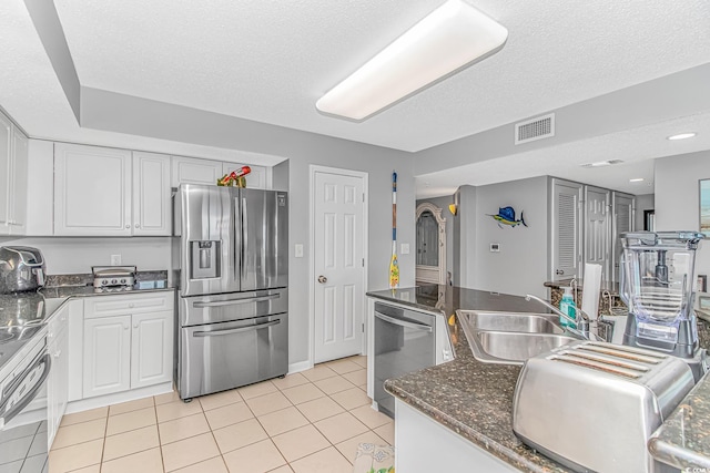 kitchen with light tile patterned floors, stainless steel appliances, visible vents, white cabinetry, and a sink