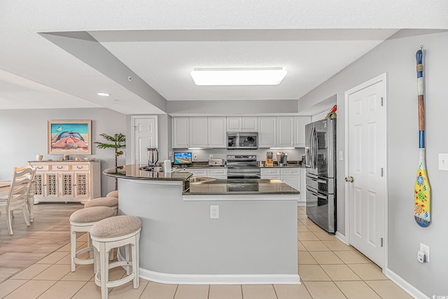 kitchen with light tile patterned flooring, stainless steel appliances, a kitchen breakfast bar, white cabinets, and dark countertops