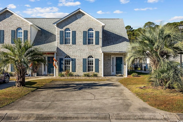 view of front of home featuring brick siding, a front lawn, and roof with shingles