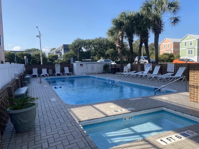 community pool with fence, a hot tub, and a patio