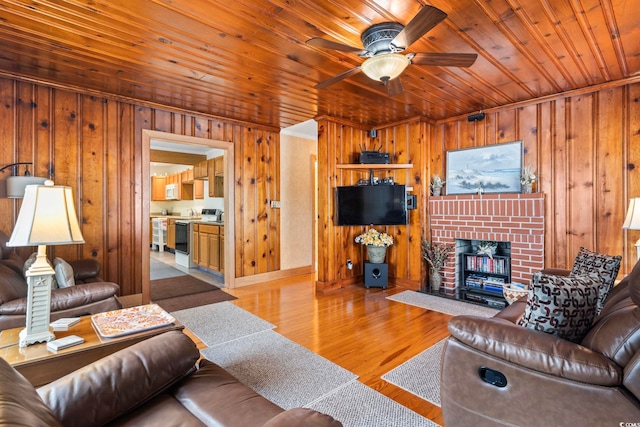 living area with ceiling fan, wooden ceiling, wooden walls, a fireplace, and wood finished floors