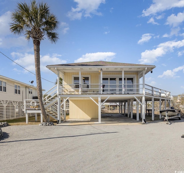 coastal home with covered porch, roof with shingles, driveway, and stairs