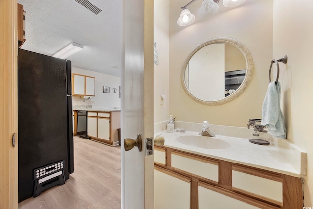 bathroom featuring a textured ceiling, vanity, wood finished floors, and visible vents