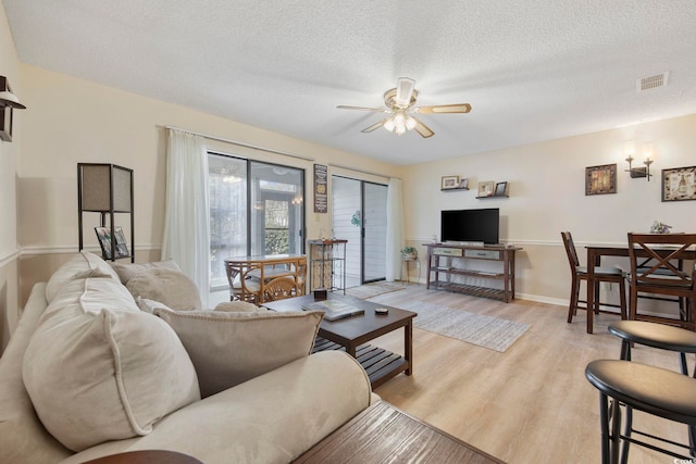 living room with a textured ceiling, visible vents, baseboards, a ceiling fan, and light wood-type flooring