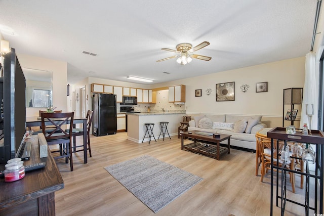 living room with light wood-type flooring, visible vents, ceiling fan, and a textured ceiling