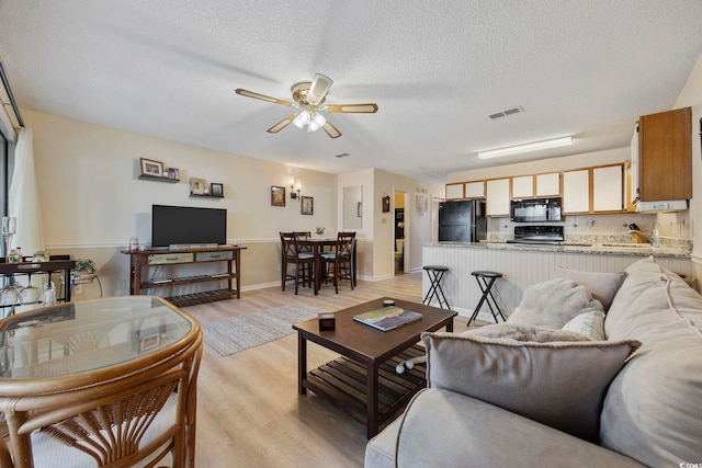 living room featuring ceiling fan, a textured ceiling, visible vents, baseboards, and light wood-style floors