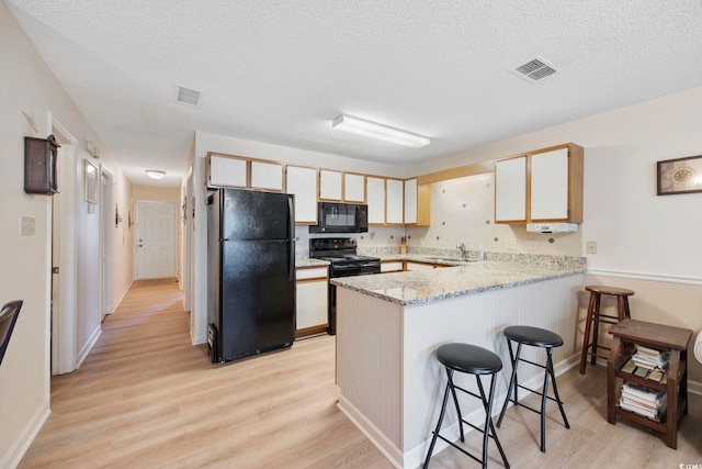 kitchen featuring light wood finished floors, visible vents, a peninsula, black appliances, and a sink