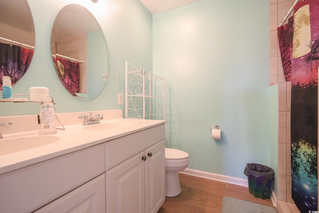 full bathroom with double vanity, toilet, wood finished floors, and a sink