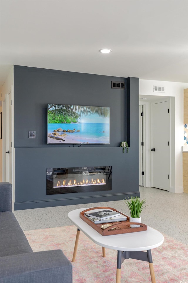 living area with a glass covered fireplace, visible vents, recessed lighting, and speckled floor