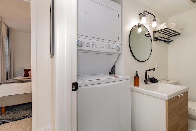 clothes washing area with stacked washer and clothes dryer, a sink, and laundry area