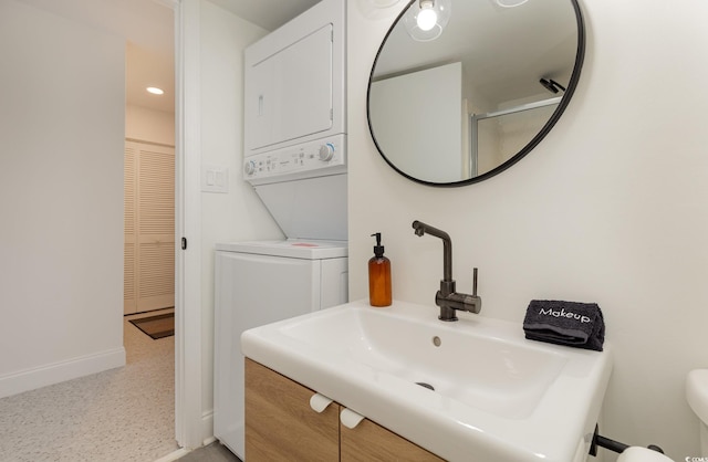 bathroom with a sink, baseboards, toilet, and stacked washer / dryer