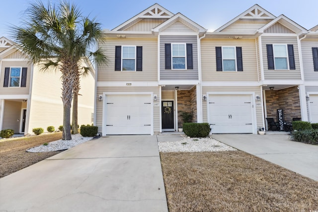 townhome / multi-family property with an attached garage, driveway, board and batten siding, and stone siding