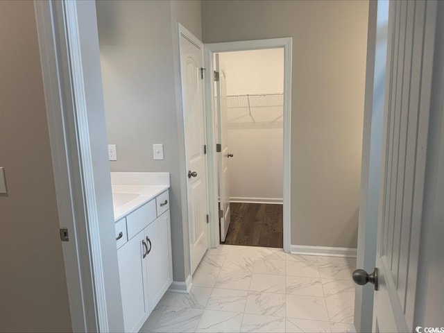 bathroom featuring marble finish floor, vanity, a walk in closet, and baseboards