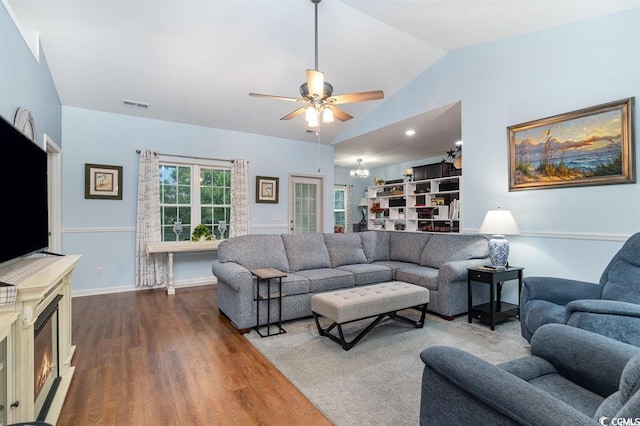 living room featuring lofted ceiling, ceiling fan, dark wood-type flooring, visible vents, and a lit fireplace