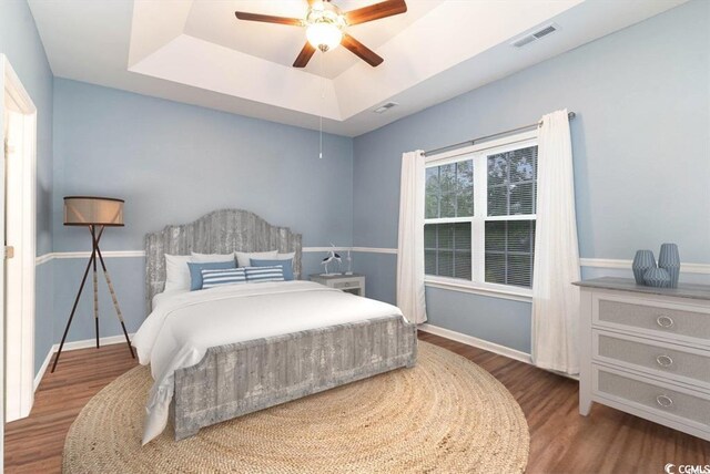 bedroom with a tray ceiling, visible vents, baseboards, and wood finished floors