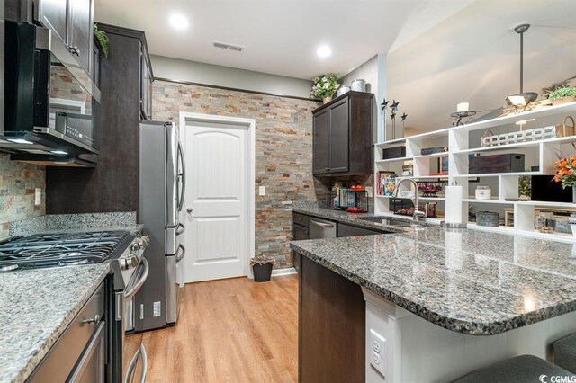 kitchen featuring appliances with stainless steel finishes, stone counters, light wood-style floors, and tasteful backsplash