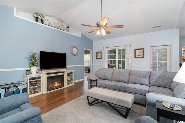 living area with lofted ceiling, ceiling fan, wood finished floors, visible vents, and a glass covered fireplace