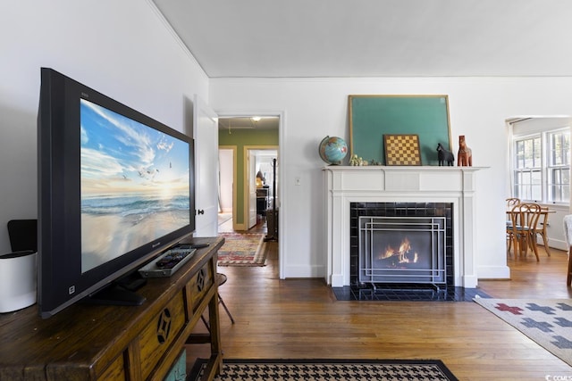 living room featuring a tiled fireplace, crown molding, wood finished floors, and baseboards