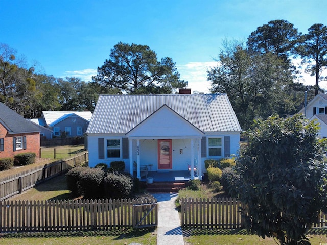 bungalow-style house with a fenced front yard, a chimney, metal roof, and a porch