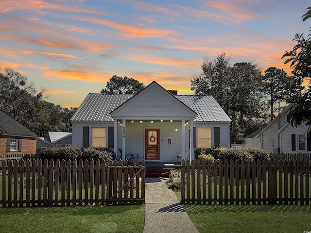 bungalow-style house with metal roof, a porch, a fenced front yard, and a gate